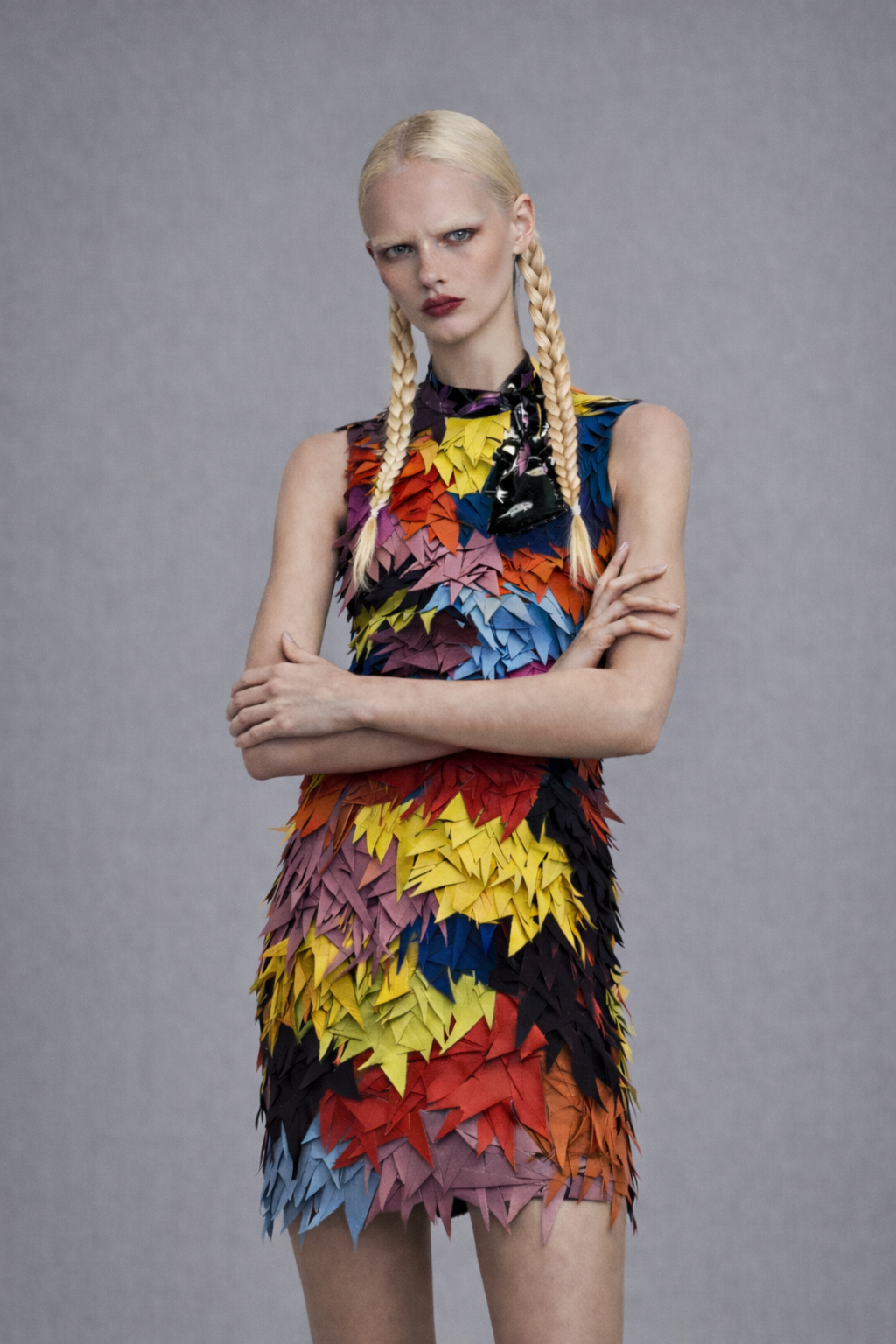 Model wearing a colorful, hand cut leather layered sheath dress with dark scarf against a gray background