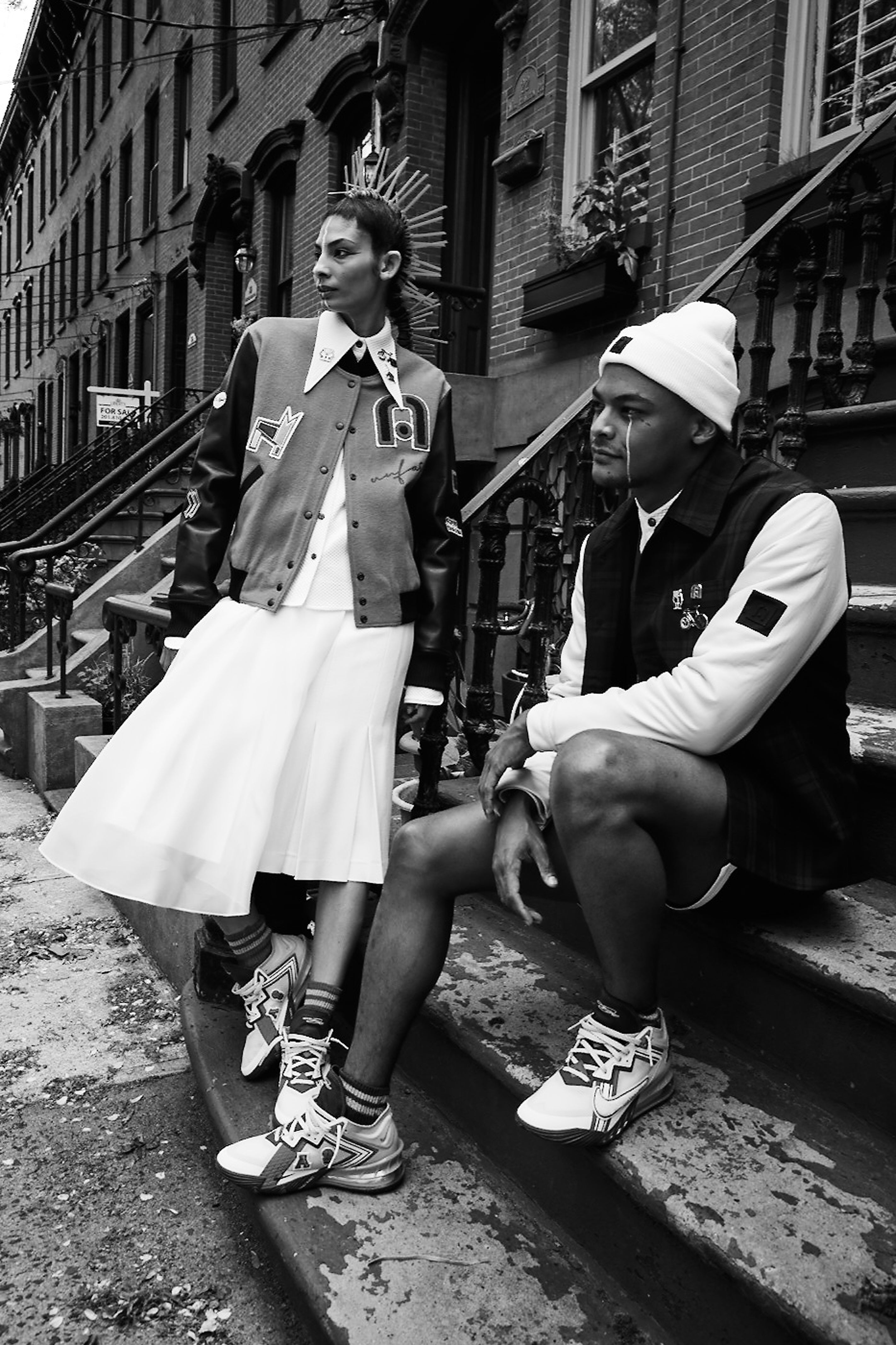 Two individuals sitting on a set of stairs in an urban setting wearing basketball sneakers