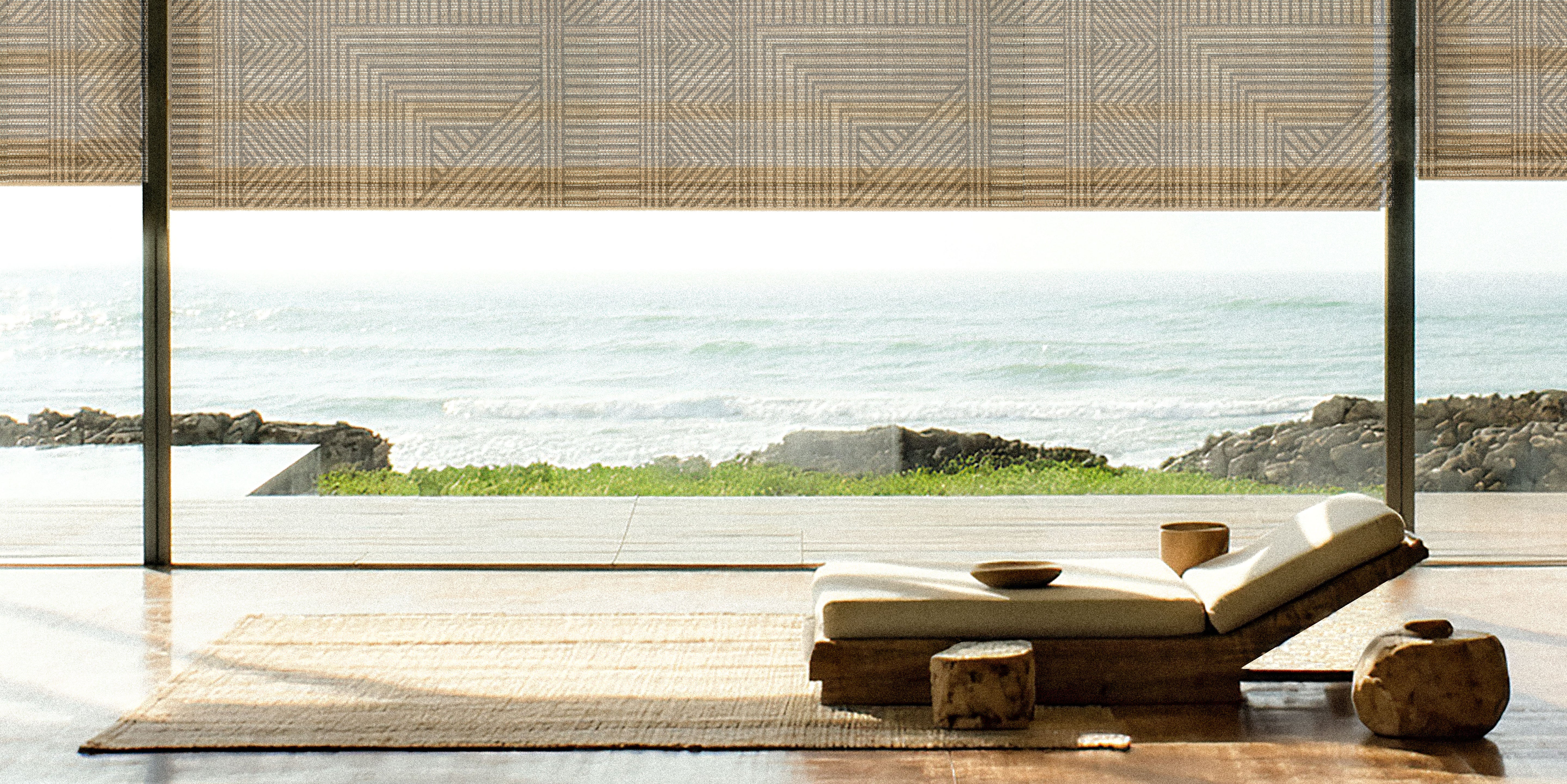 Modern interior with a lounge chair and scenic view of water and land with The Shade Store x Mimi Plange window treatment in African inspired print