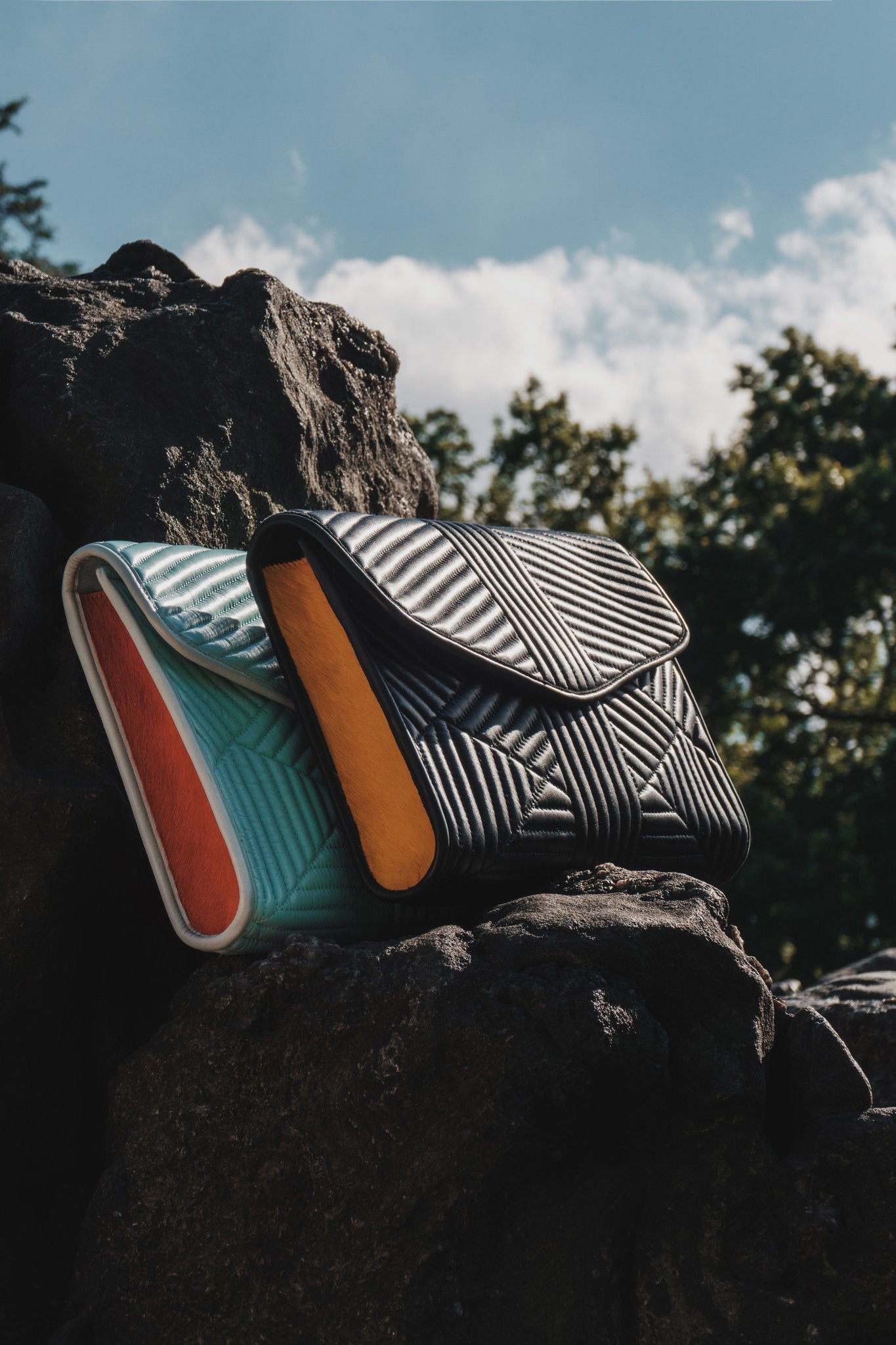 Two patterned leather quilted bags on a rock with a natural background