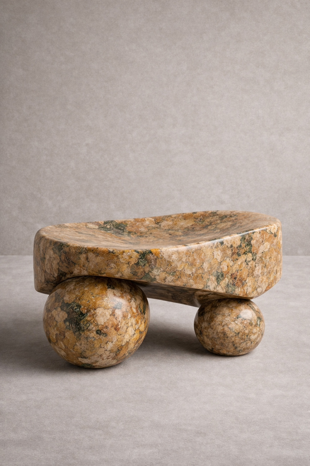Stone sculpture ottoman with a large flat stone on top and two spherical stones below on a gray background