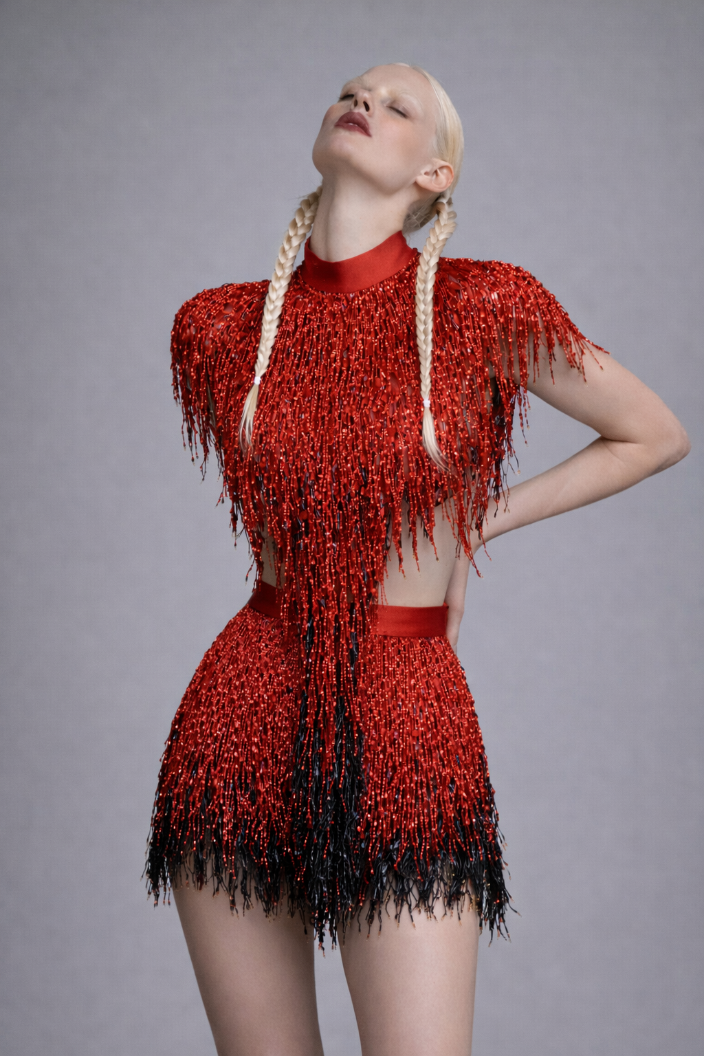 Woman wearing a red and black fringed cape and mini skirt against a gray background
