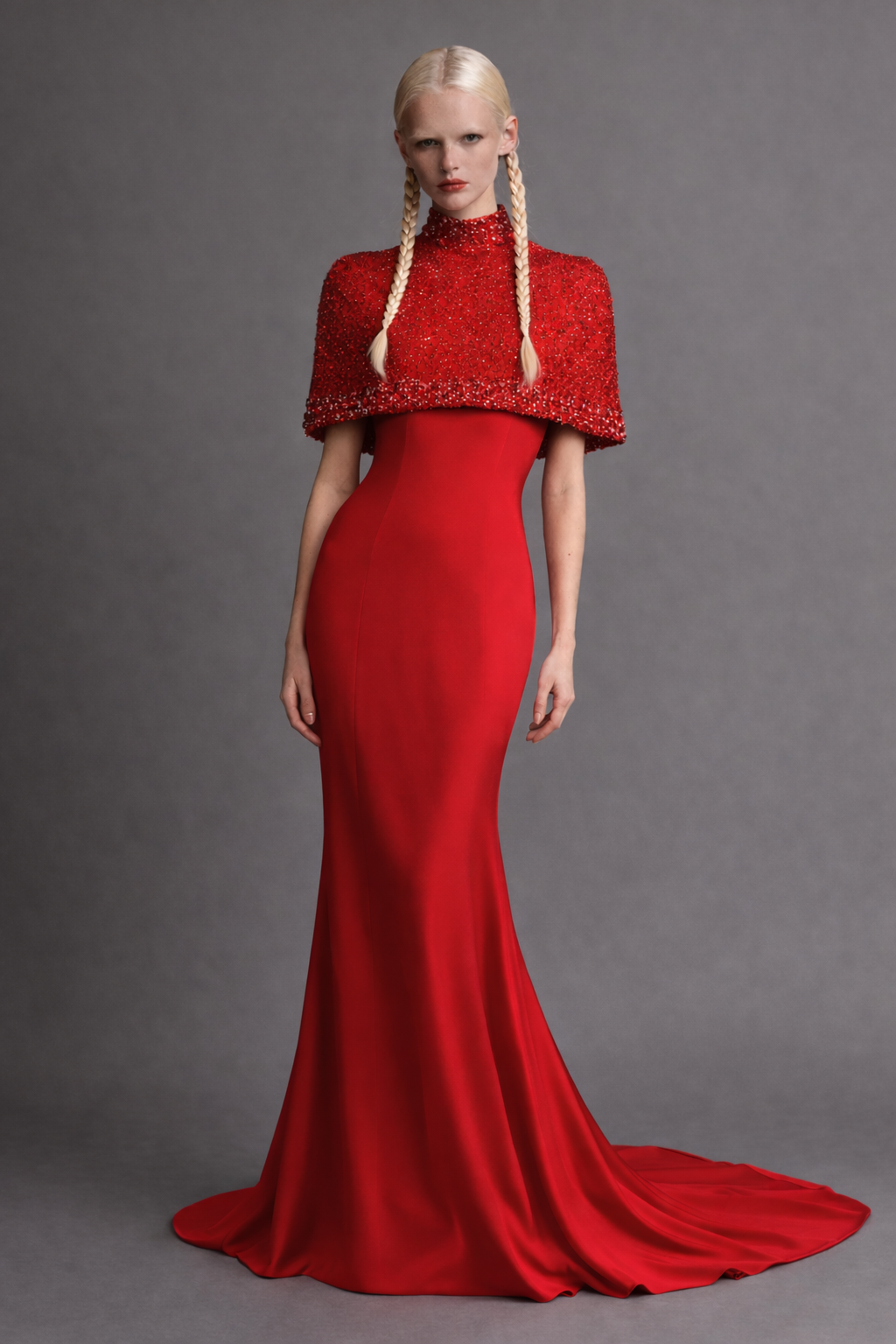 Woman wearing a red evening gown with a matching beaded and embroidered cape against a gray background