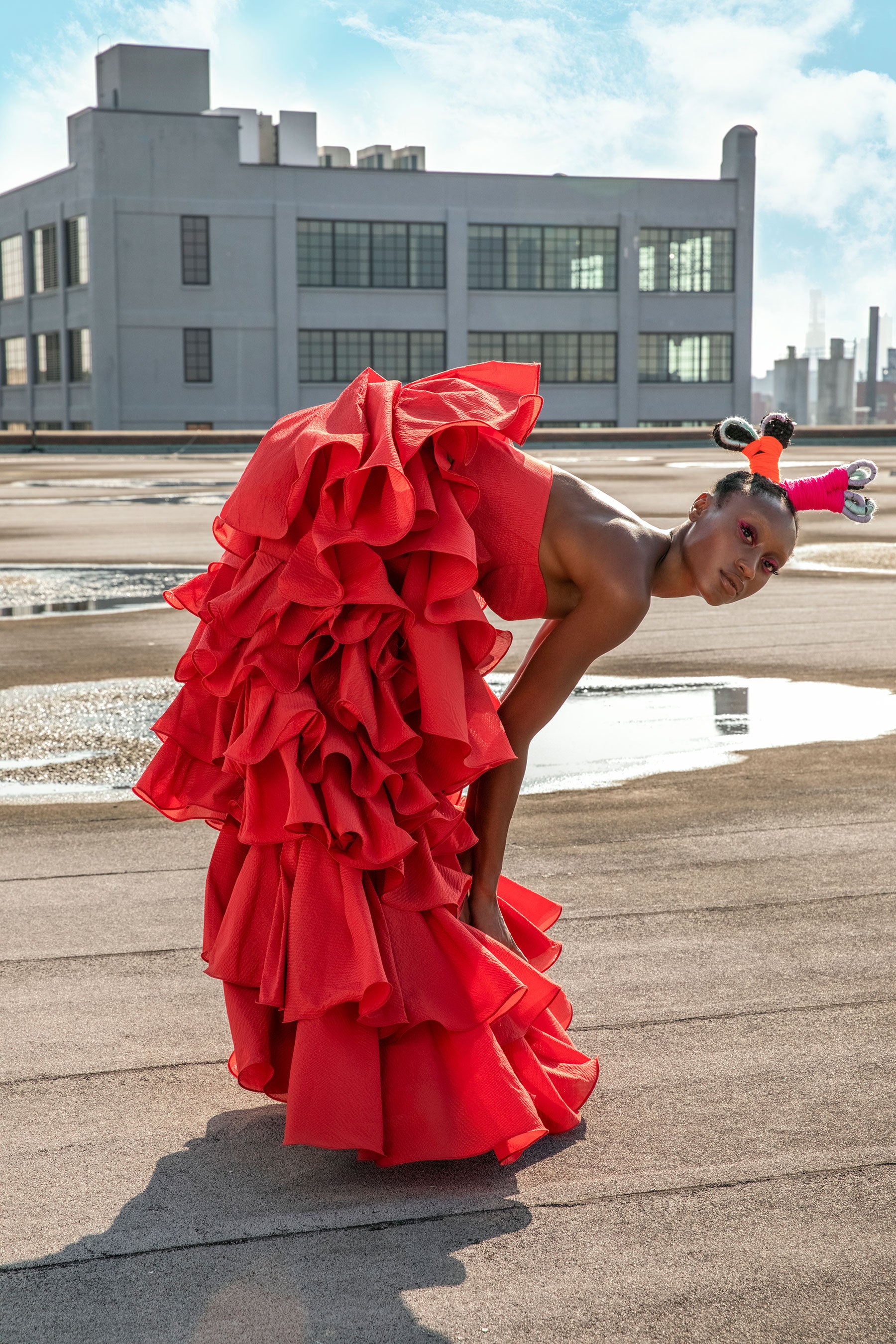 A model on a rooftop with sculpted hair wears a long Maxi Ruffle Skirt and Red bustier by Mimi Plange