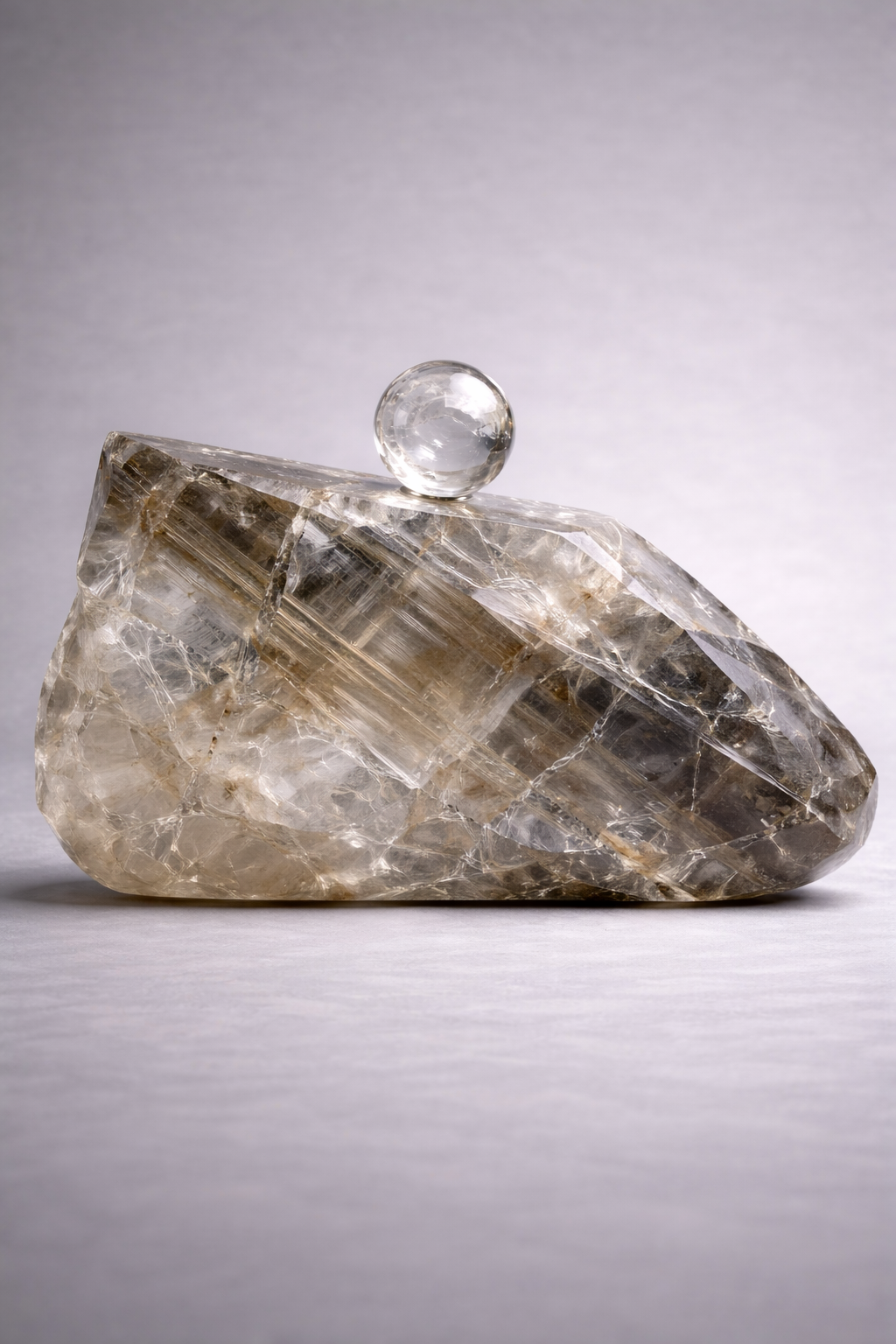 Crystal rock clutch bag with a clear sphere on top against a gray background