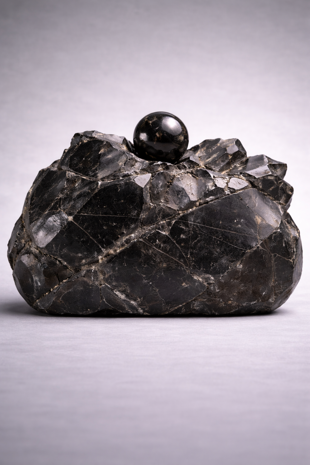 Decorative black stone clutch bag with a spherical object on top against a gray background