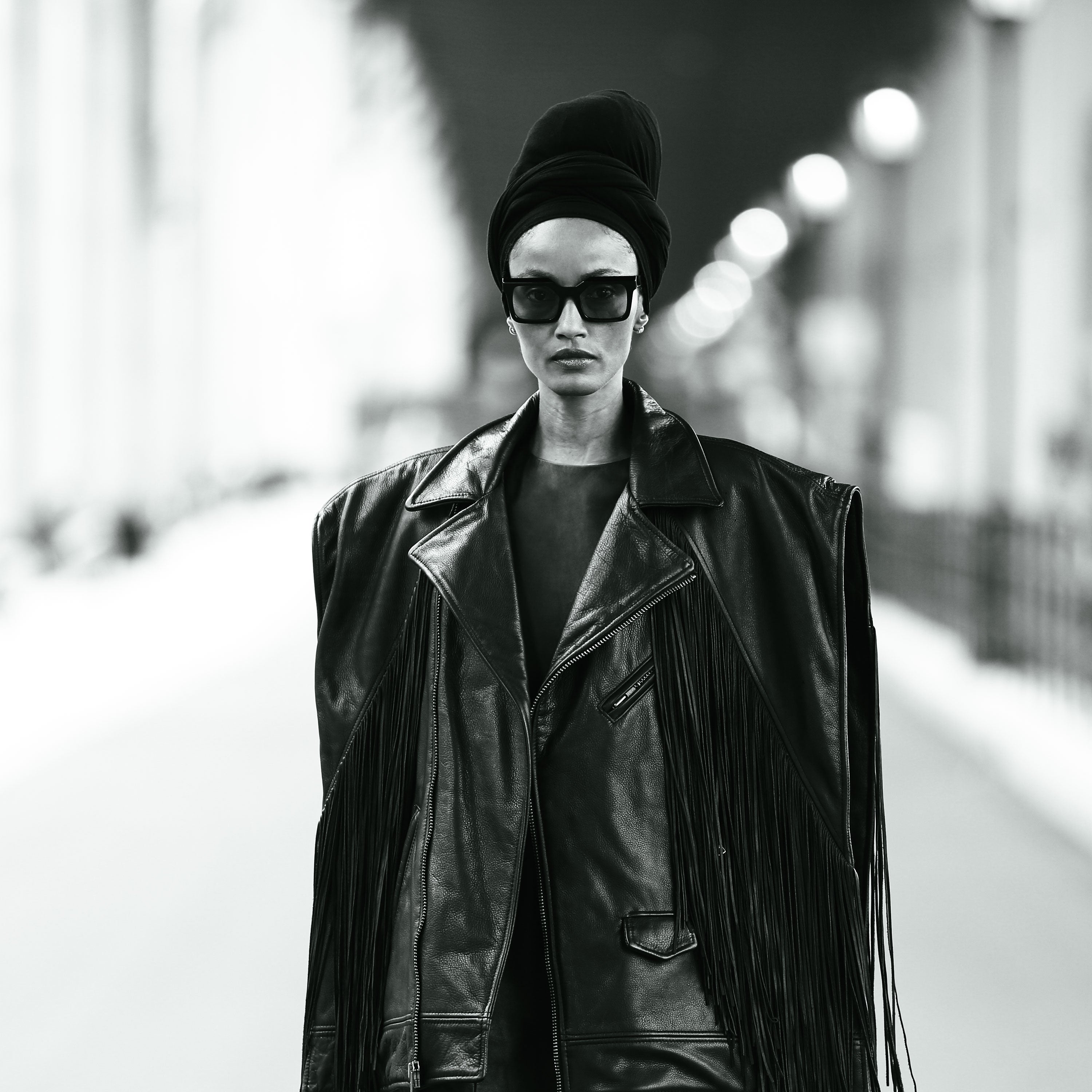 Model Paradis Winslet wearing a black leather fringe jacket by Mimi Plange and sunglasses with a blurred background