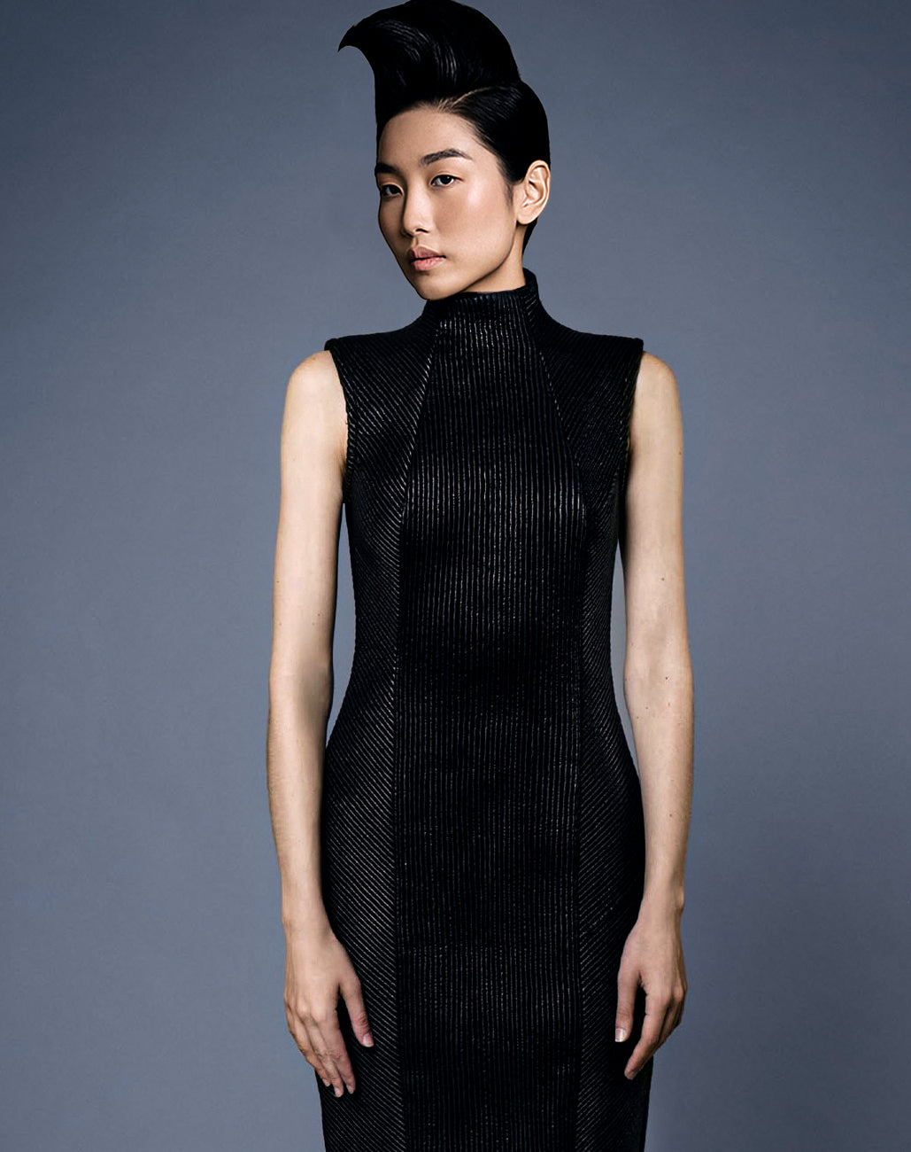 Woman wearing a black sleeveless leather trapunto embroidery dress inspired by African Scarification against a gray background