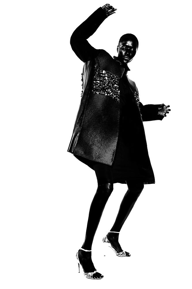 Black and white image of a model wearing a long leather coat with beading at the top on a white background