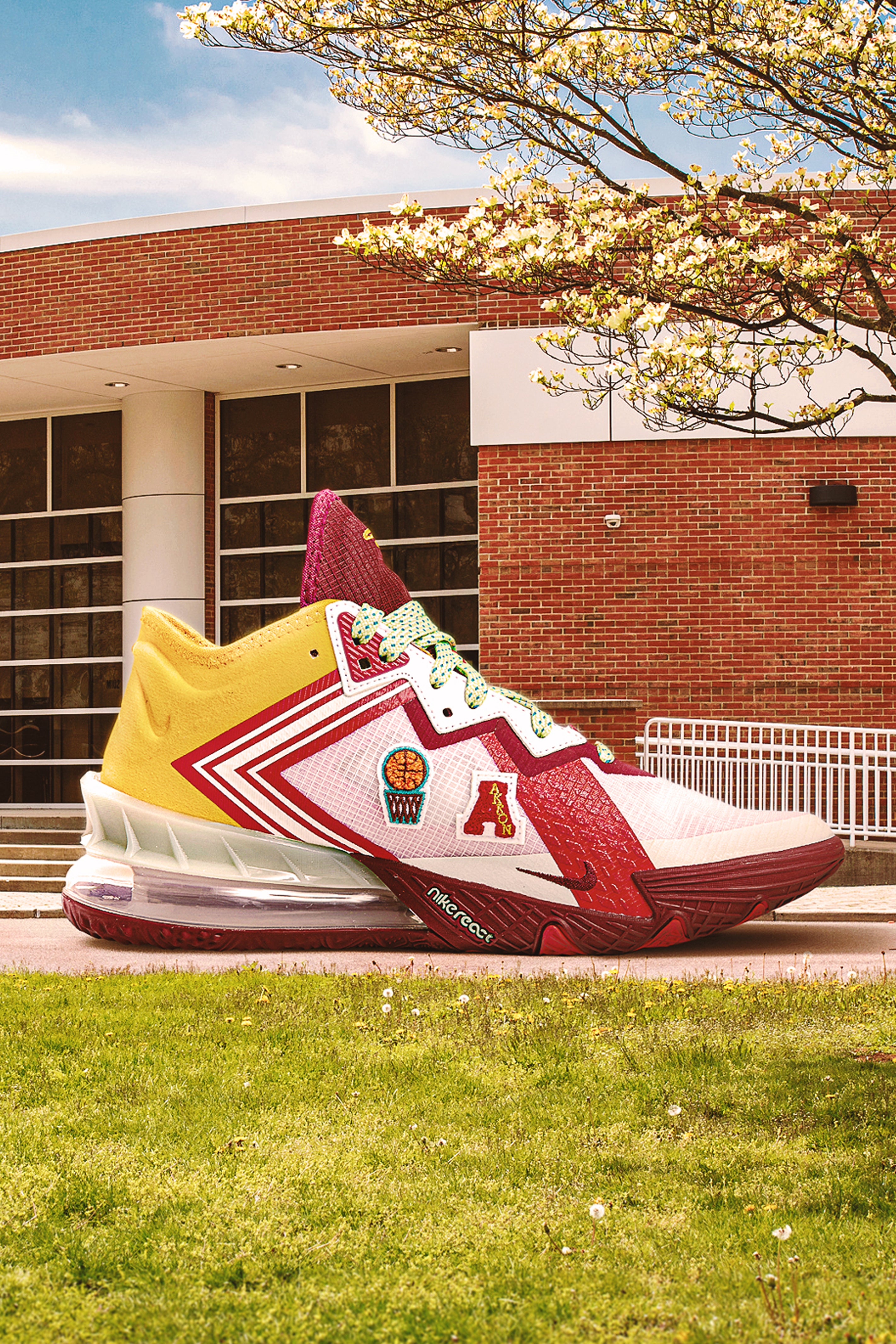 Colorful varsity basketball sneaker with patches on grass in front of a building