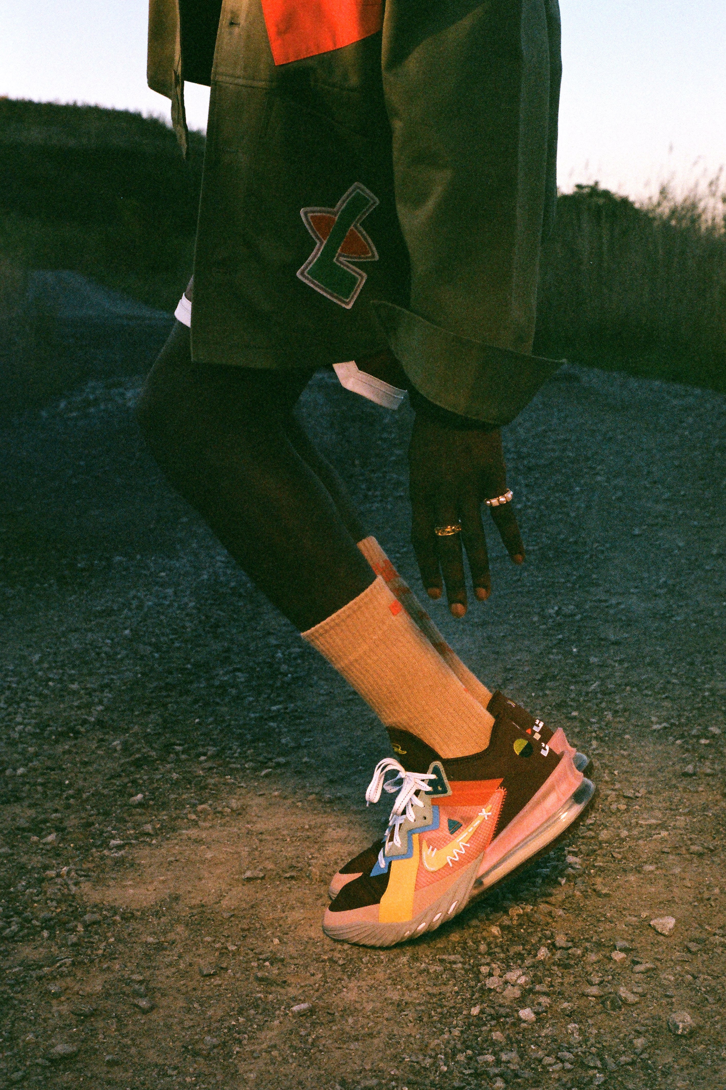 Person wearing a dark jacket with a logo, bright socks, and colorful sneakers on a road.