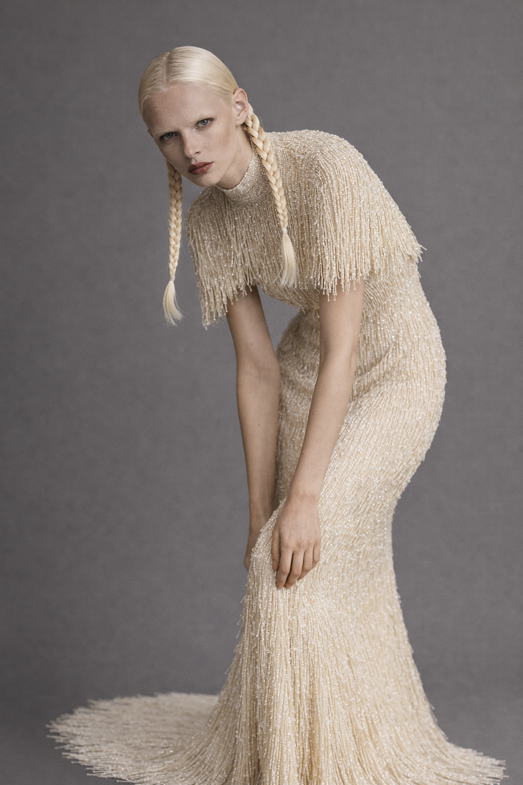 Woman wearing a long, fringed beige evening gown against a gray background