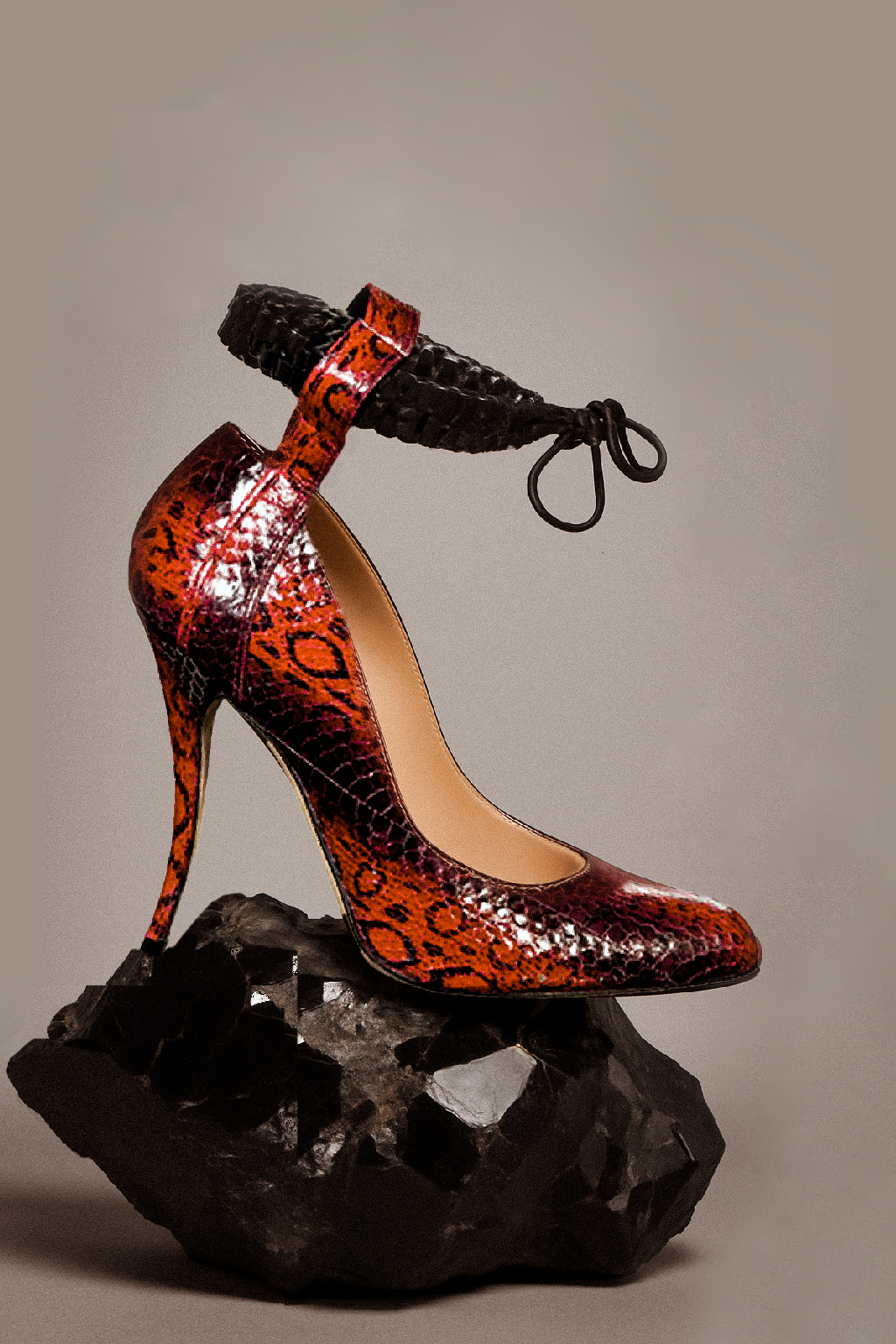 Red snakeskin High-heeled shoe braided leather anklet design, brutalita by Manolo Blahnik x Mimi Plange on a gray background