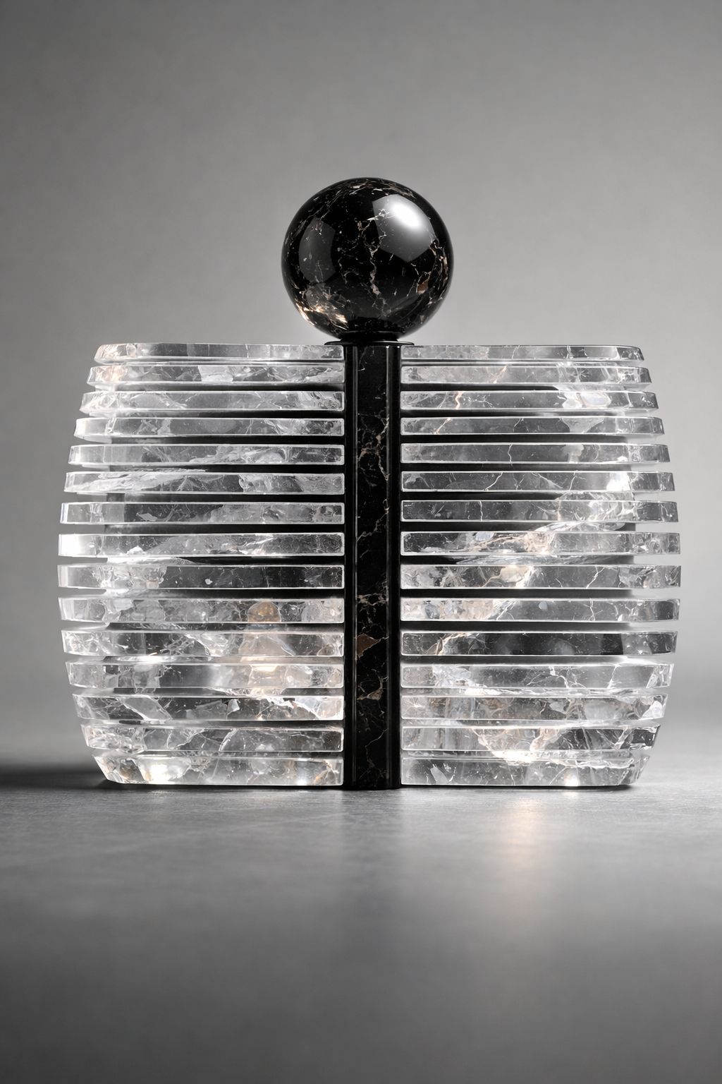 Decorative crystal clutch bag with a black sphere on top and ribbed white base against a gray background