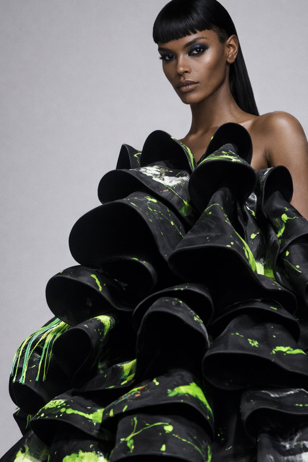 Model wearing a black and green couture hand painted ruffle gown on a gray background