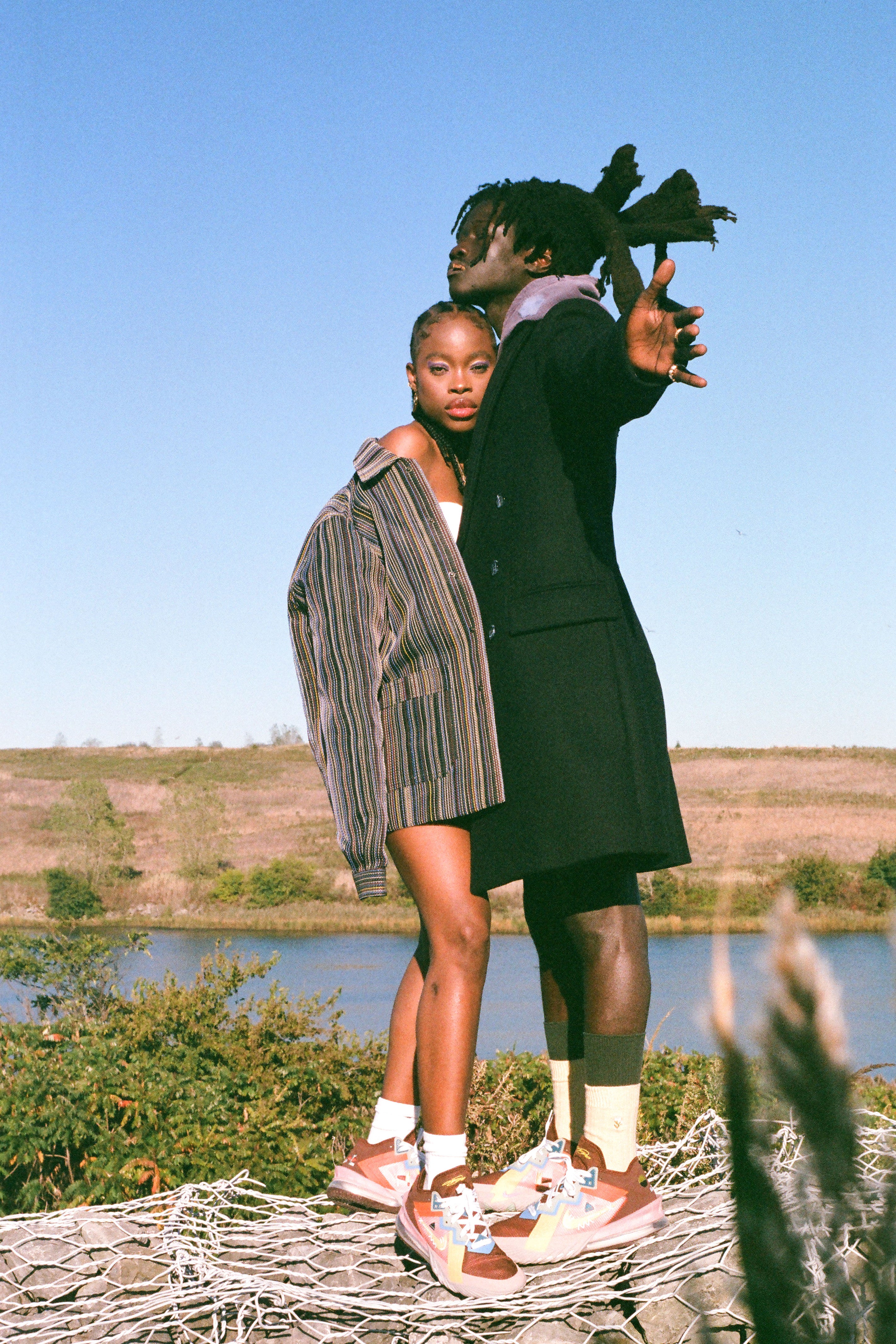 Two people wearing basketball sneakers standing on a woven mat with a scenic background of water and sky.