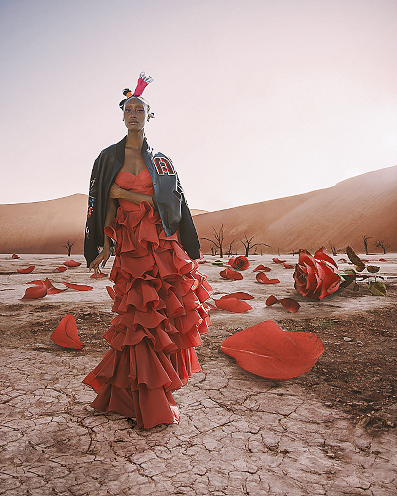 A surreal photograph of a model wearing a red ruffle gown and varsity jacket with digital red roses on the ground, in the Namibia desert.
